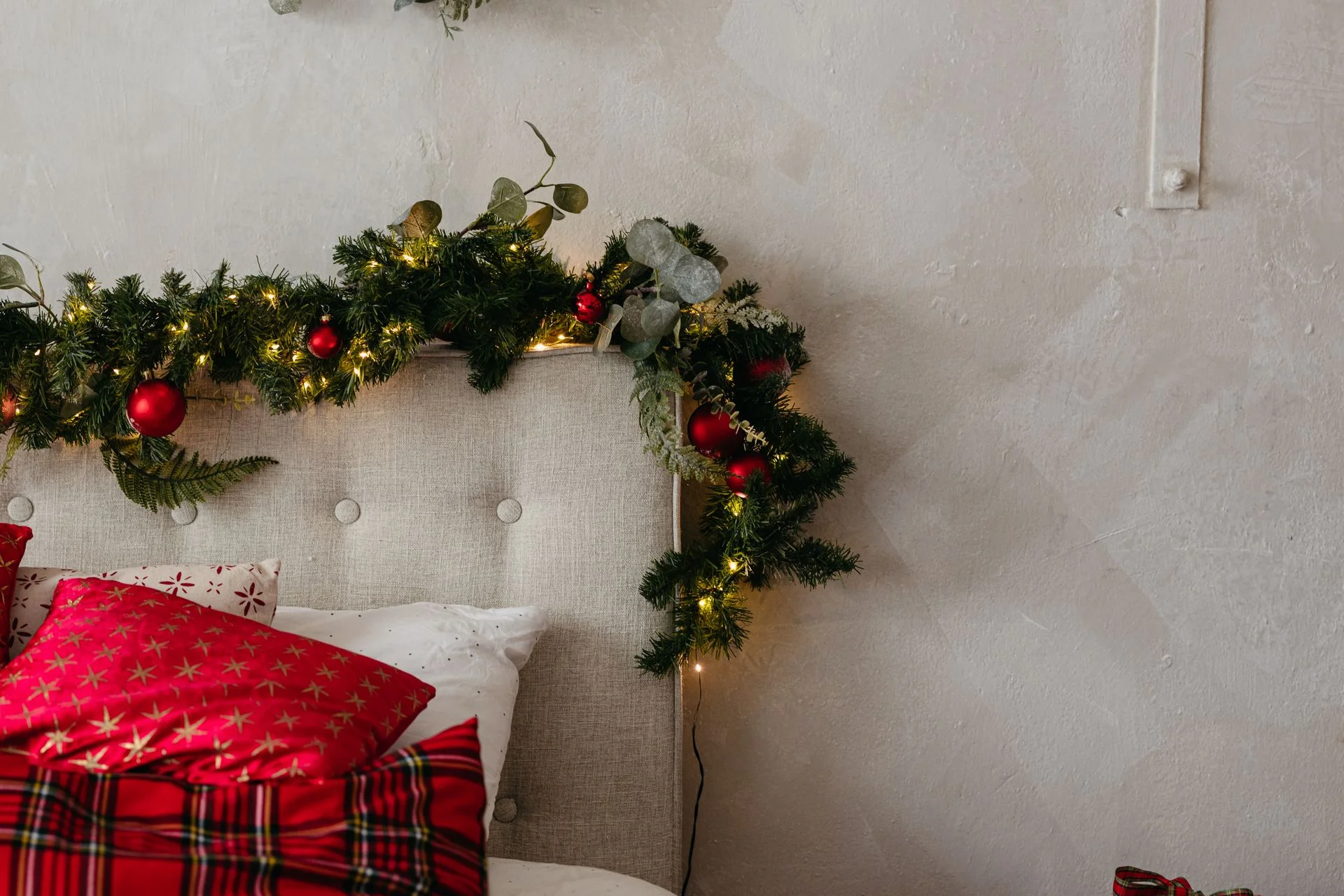 Cozy rustic christmas bedroom with red plaid pillows and a lit pine garland over the headboard