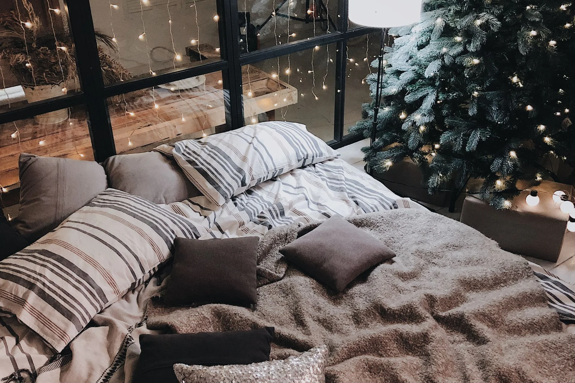 A cozy bedroom with a small christmas tree beside the bed and warm string lights