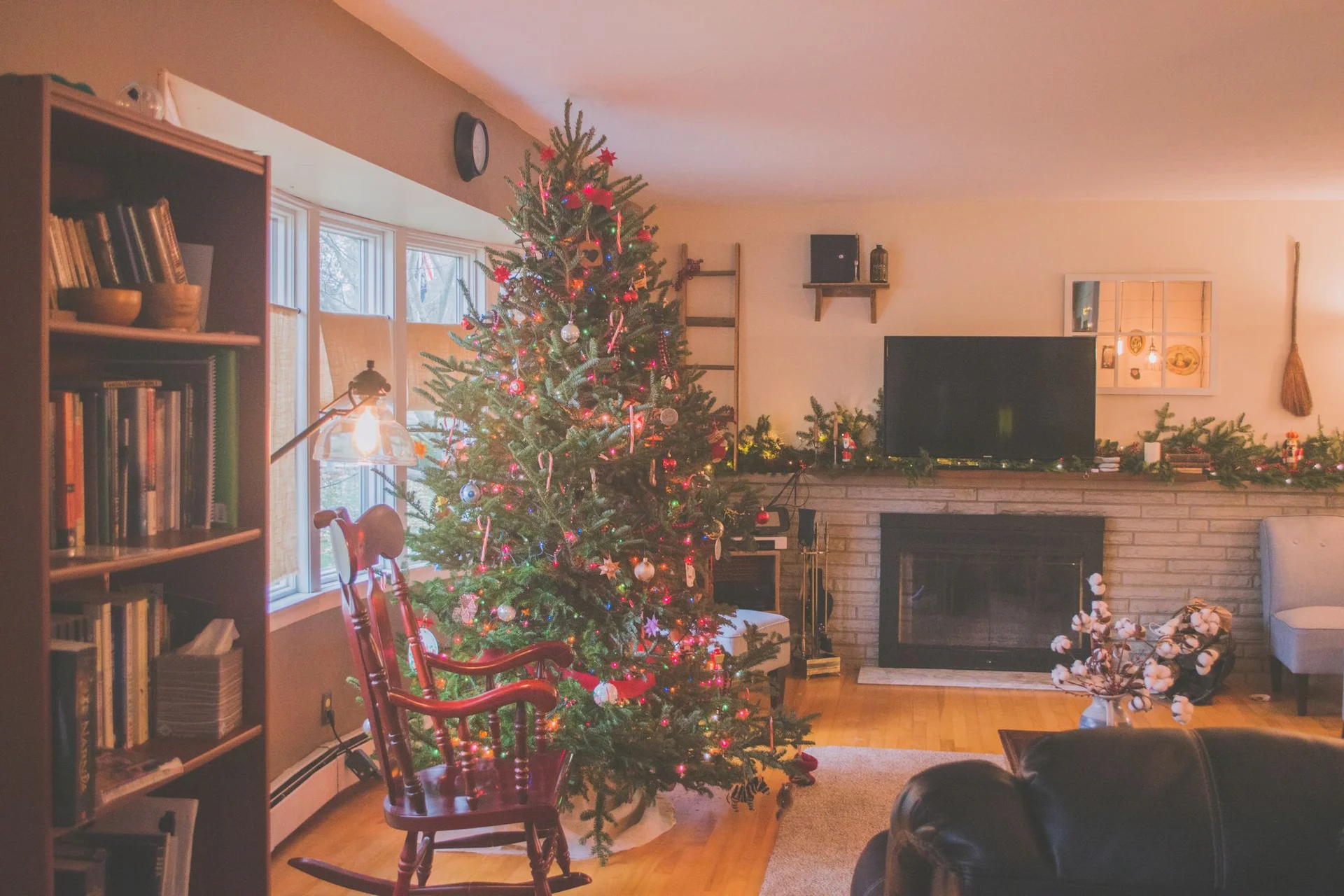 A lit christmas tree beside a window in a warm, cozy room
